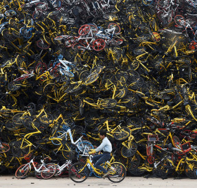 A worker rides a shared bicycle past piled-up shared bikes at a vacant lot in Xiamen, Fujian province, China December 13, 2017. Picture taken December 13, 2017. REUTERS/Stringer  ATTENTION EDITORS - THIS IMAGE WAS PROVIDED BY A THIRD PARTY. CHINA OUT.     TPX IMAGES OF THE DAY - RC16B19B1FA0