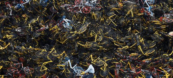 A worker rides a shared bicycle past piled-up shared bikes at a vacant lot in Xiamen, Fujian province, China December 13, 2017. Picture taken December 13, 2017. REUTERS/Stringer  ATTENTION EDITORS - THIS IMAGE WAS PROVIDED BY A THIRD PARTY. CHINA OUT.     TPX IMAGES OF THE DAY - RC16B19B1FA0